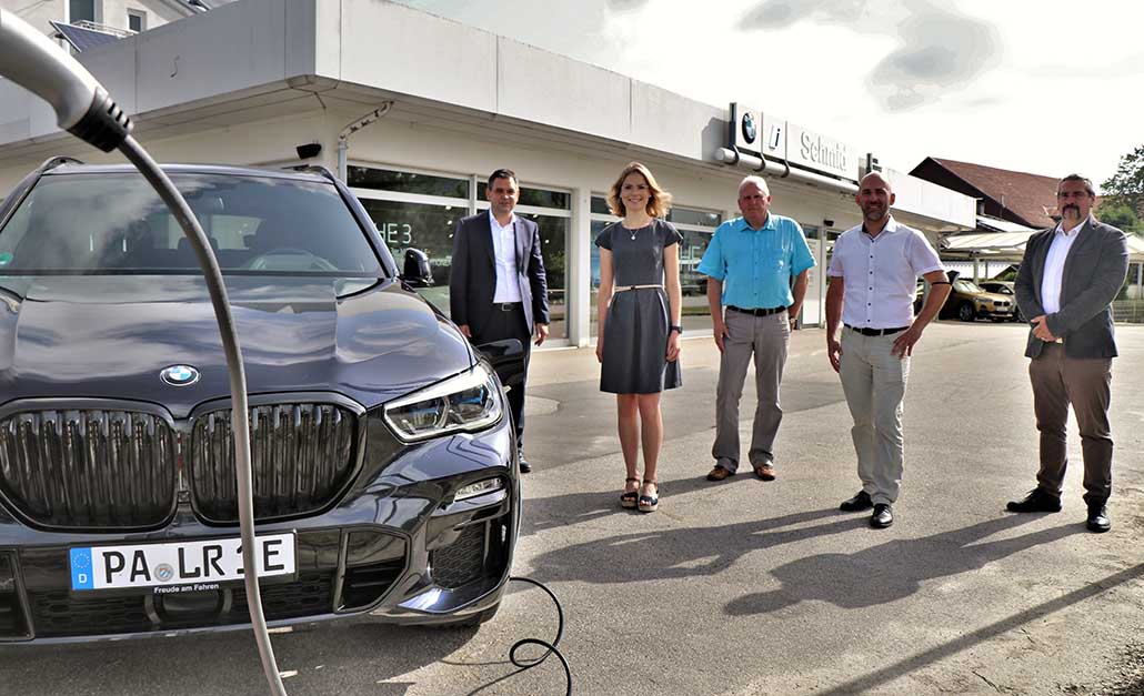 Offizielle Übergabe eines BMW X5 mit Hybridantrieb durch Gregor Leebmann, Filialleiter bei BMW SCHMID Service GmbH in Hauzenberg/Jahrdorf und Harald Höpfler, Teamleiter Verkauf SCHMID Service Gmbh an Landrat Raimund Kneidinger. Magdalena Fassbinder und Andreas Hansen. Der BMW X5 mit E-Antrieb wird an einer Ladesäule aufgeladen. Hintergrund: Verkaufsgebäude BMW SCHMID Service GmbH.