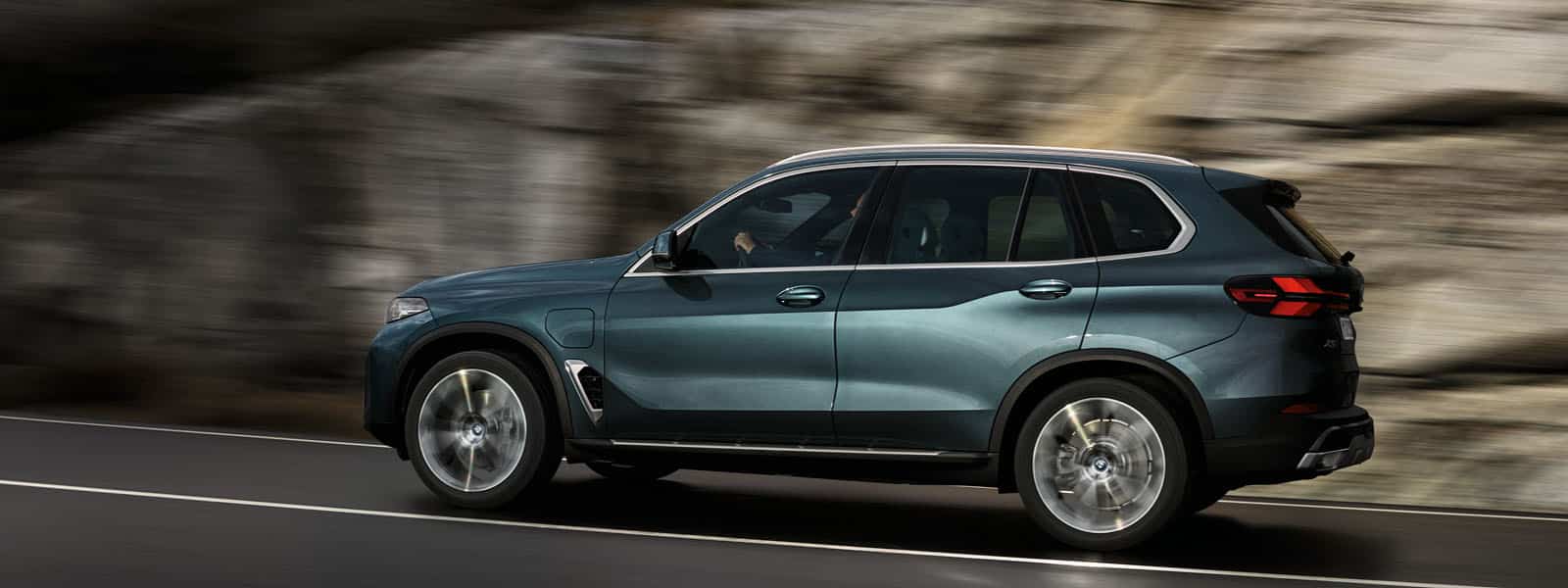 Dunkelblauer BMW X5 SUV fährt auf einer Straße mit Felswand im Hintergrund. Seitlich Fotografiert mit Überschrift: BMW PREMIUM SELECTION GARANTIE. DIE NEUEN GEBRAUCHTEN. Link blau hinterlegt: JETZT FAHRZEUG FINDEN.