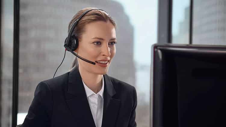 Frau mit Headset und Mikrofon lächelt während eines Gesprächs am Computer in einem Großstadtbüro.
