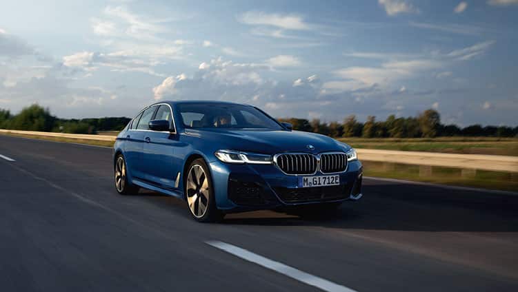 Dunkelblauer BMW fährt dynamisch auf einer Straße mit bewölktem Himmel.