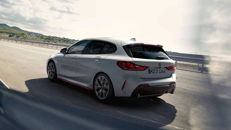 Weißer BMW 1er fährt auf einer bergigen Landstraße, Rückansicht.