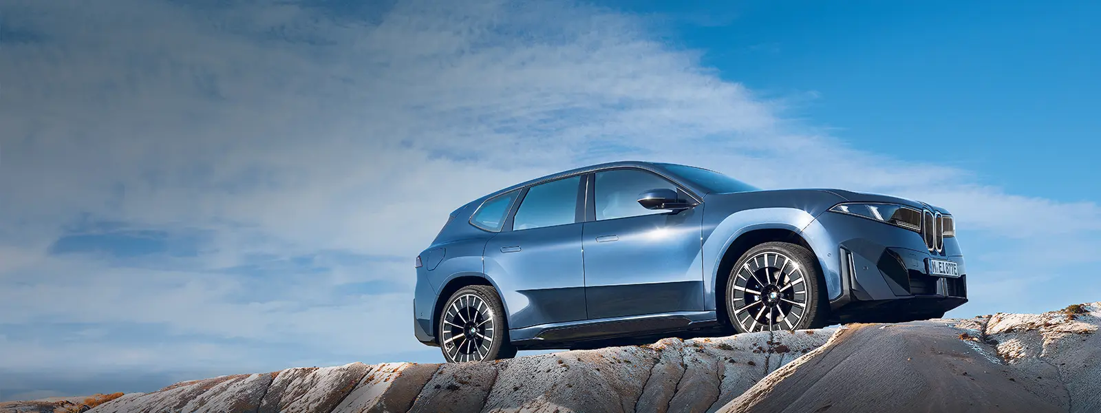 BMW iX3 seitlich fotografiert auf eine Felse.