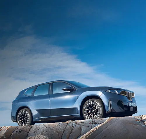 BMW iX3 seitlich fotografiert auf eine Felse.