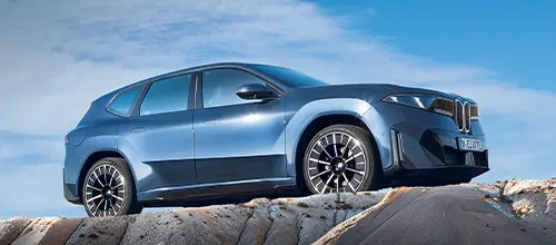 BMW iX3 seitlich fotografiert auf eine Felse.