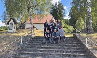 Gruppe Menschen sitzend und stehend auf eine Treppe. Im Hintergrund eine Kapelle. Motorrad Leebmann Tour Slowenien 2025.